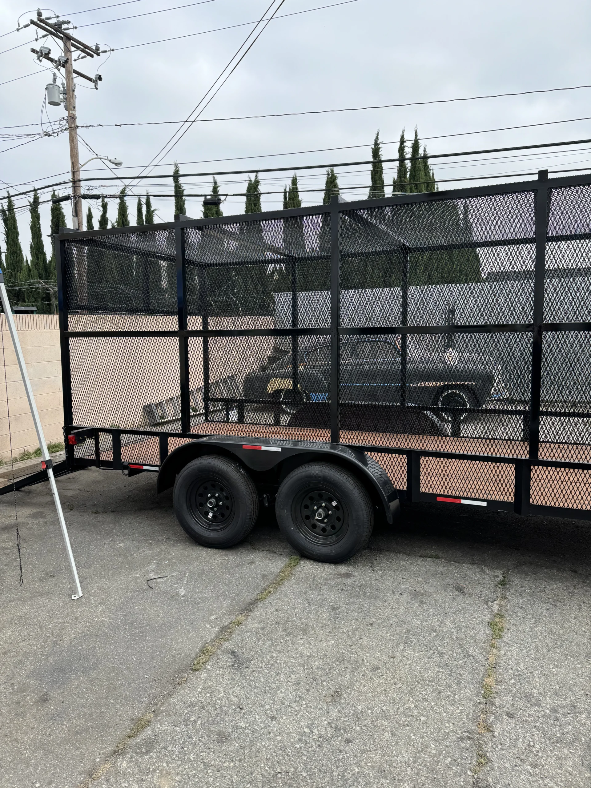 Side view of a completed tandem axle landscaping trailer with tall mesh cage walls and wood deck