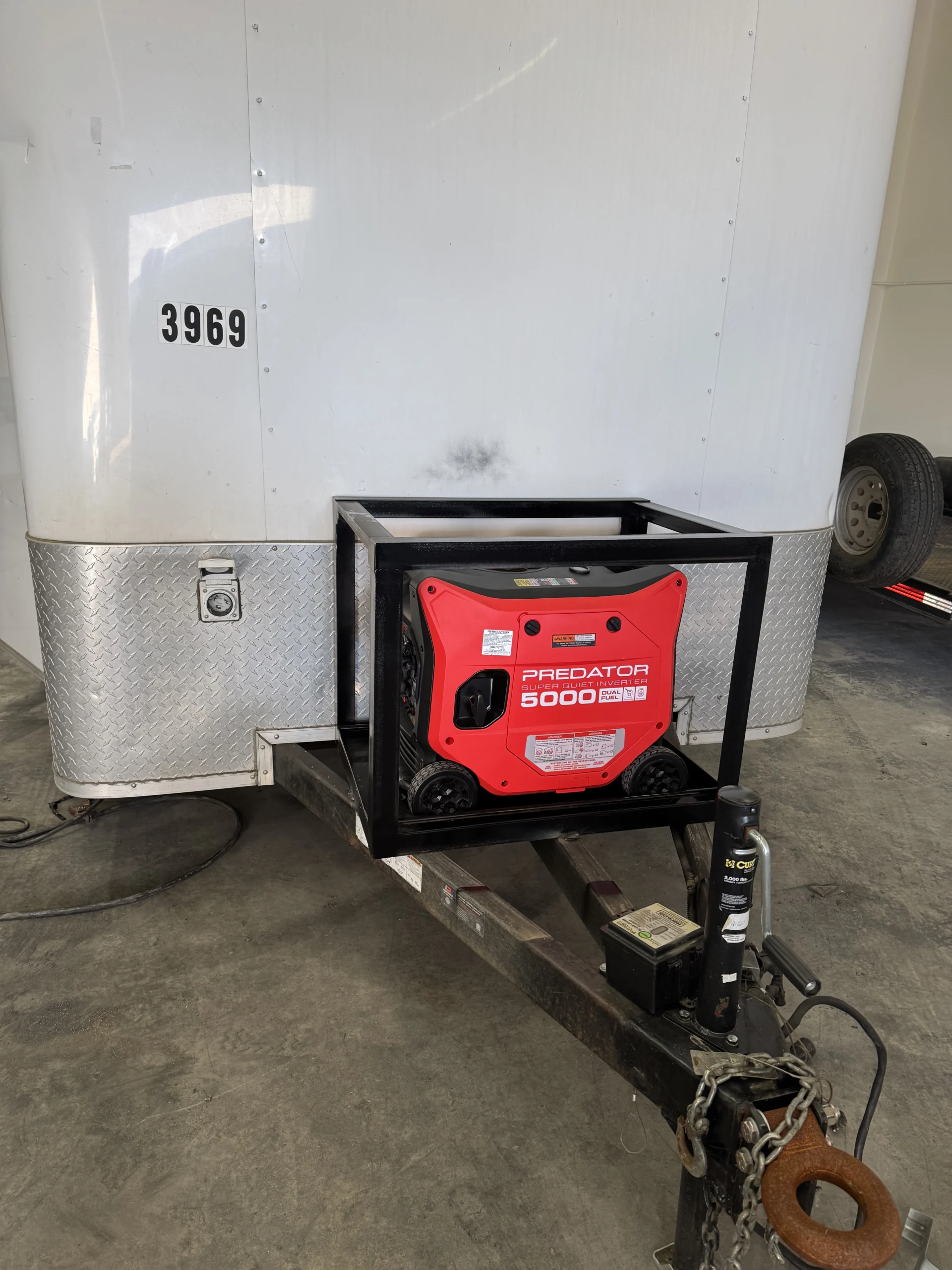 Portable generator secured in a custom welded steel cage mount on a trailer tongue